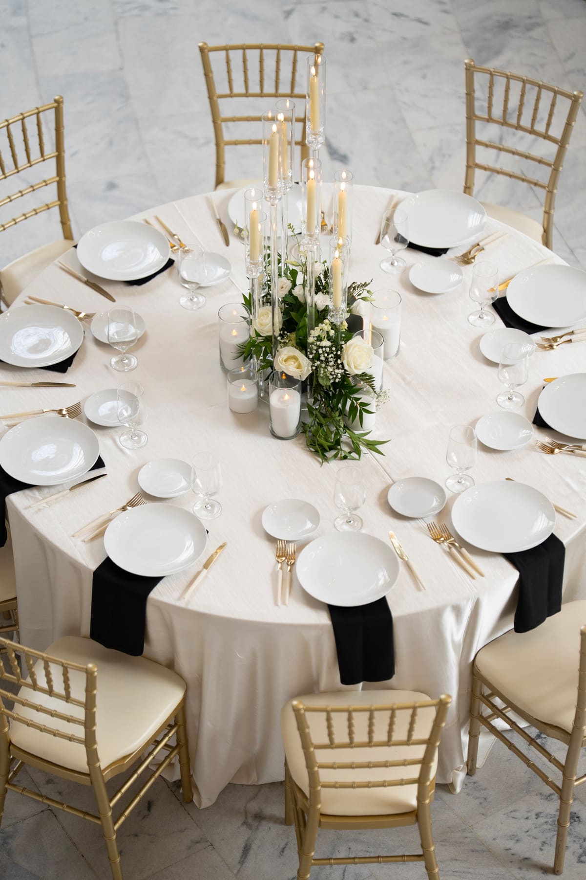 A round reception table set with gold chiavari chairs and white florals