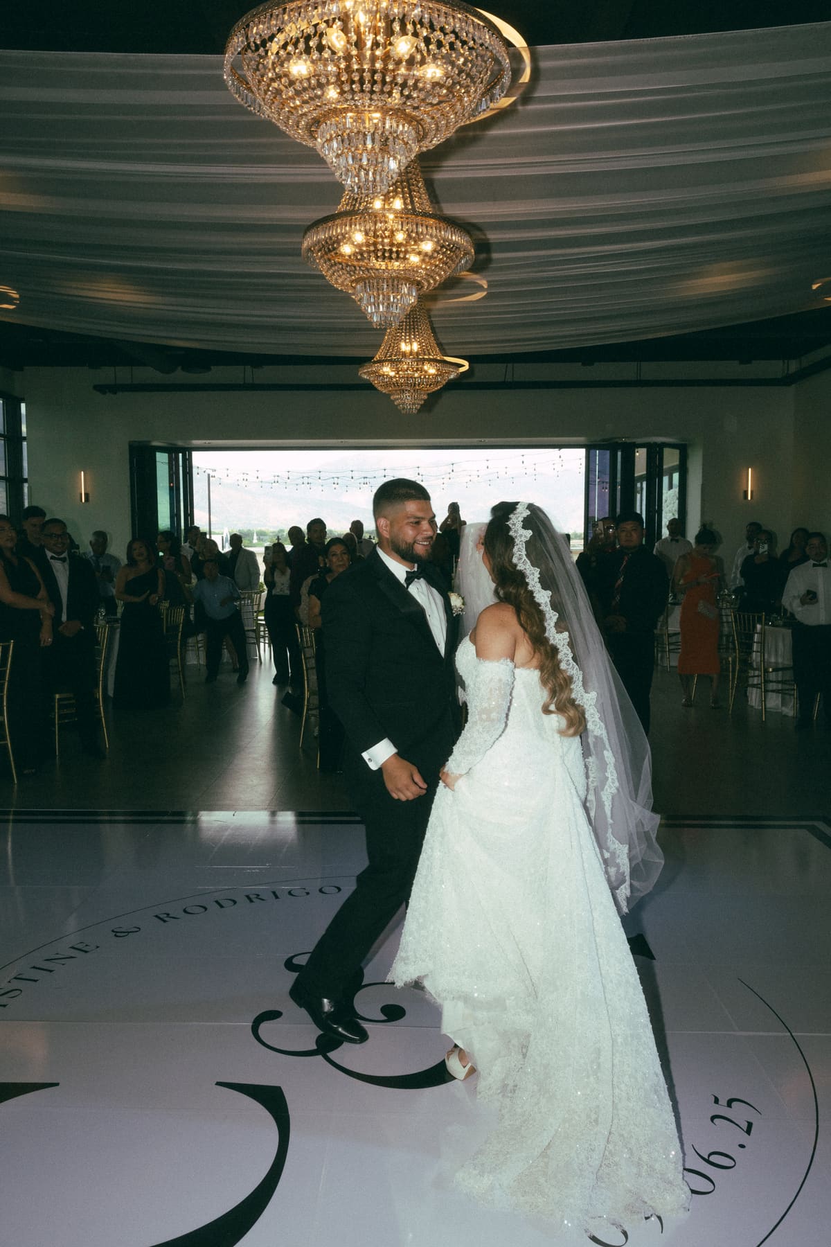 A couple entering their reception beneath a glowing crystal chandelier