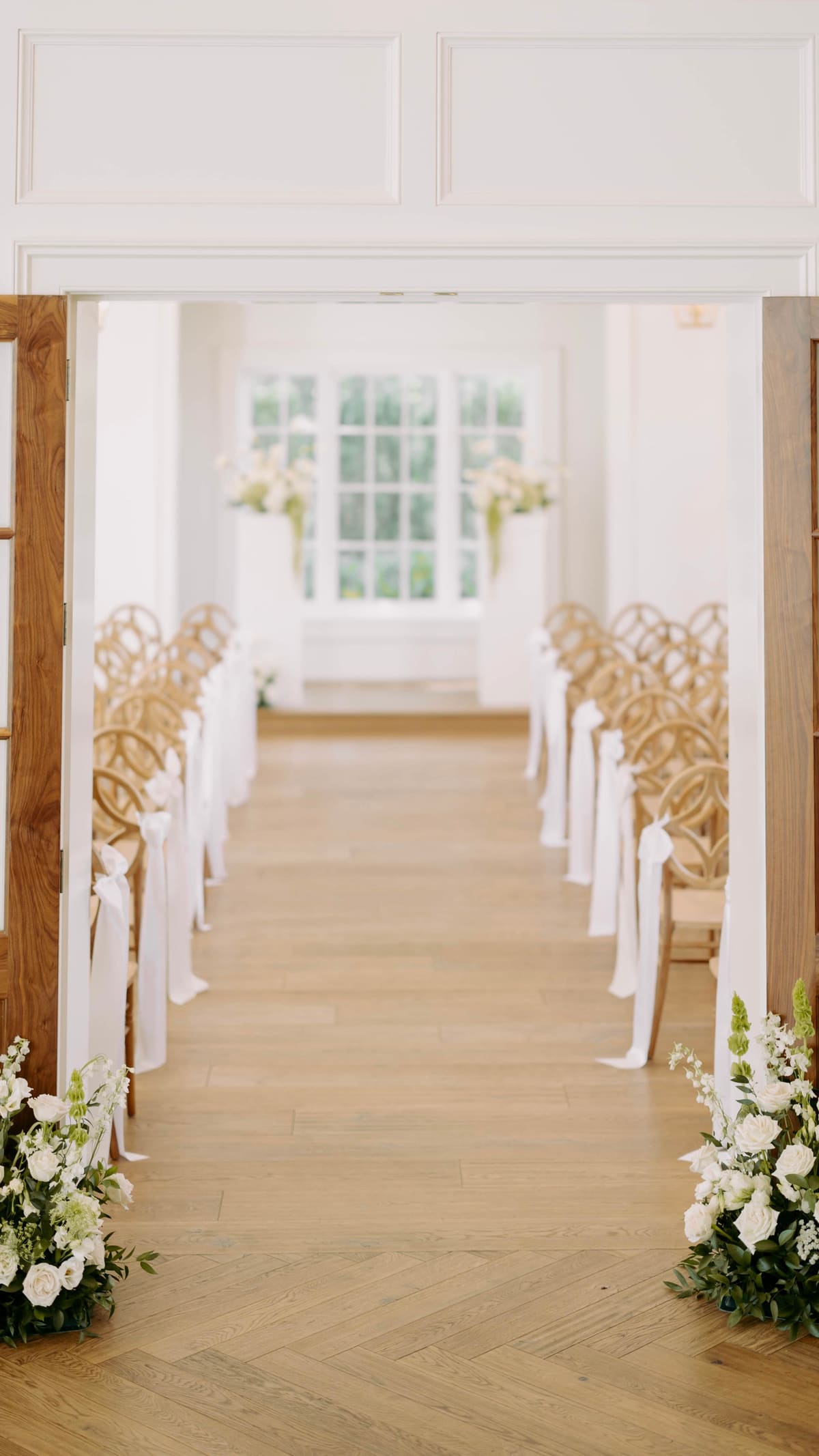 A white aisle lined with florals inside a light-filled venue